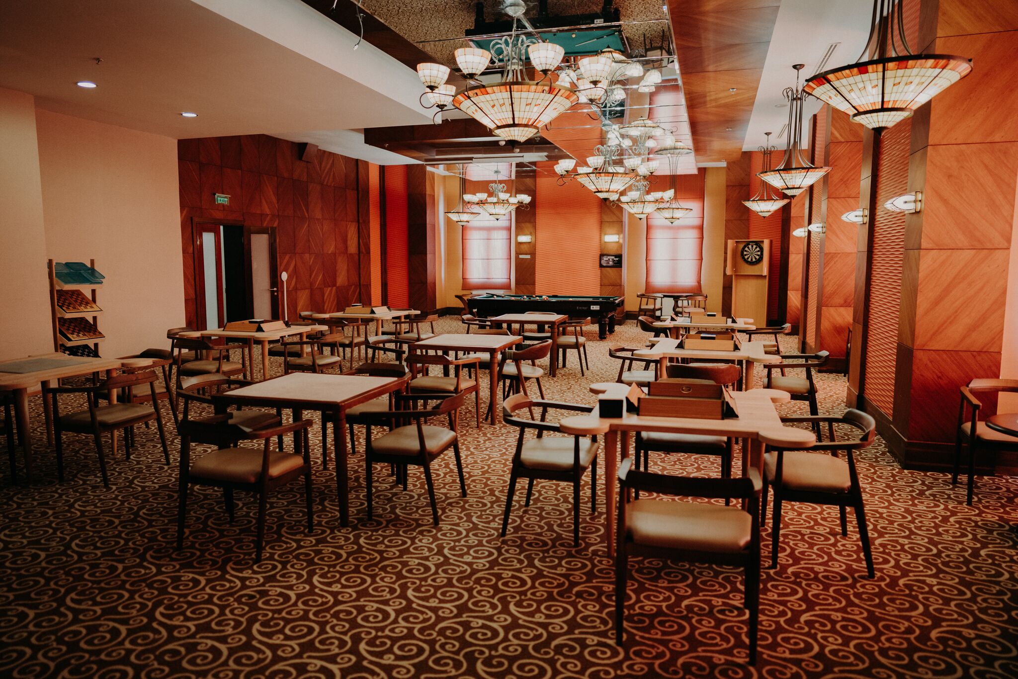 A spacious dining area with multiple tables and chairs, a pool table, and decorative lighting fixtures.