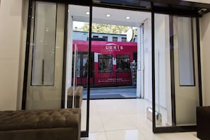 A modern building entrance with glass doors, a red storefront, and a bench inside. - The Constantine Hotel (Istanbul)