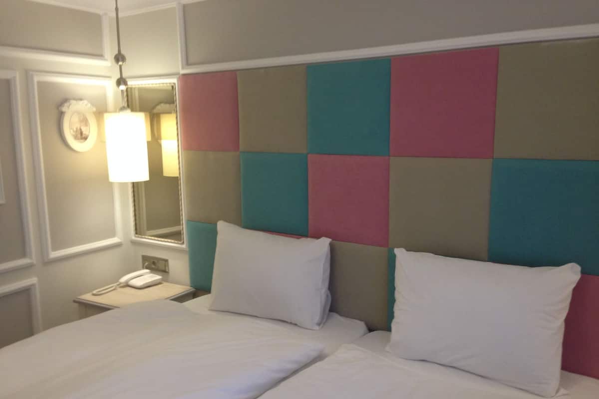 Un lit double avec du linge de lit blanc, une table de chevet avec une lampe et une tête de lit colorée.