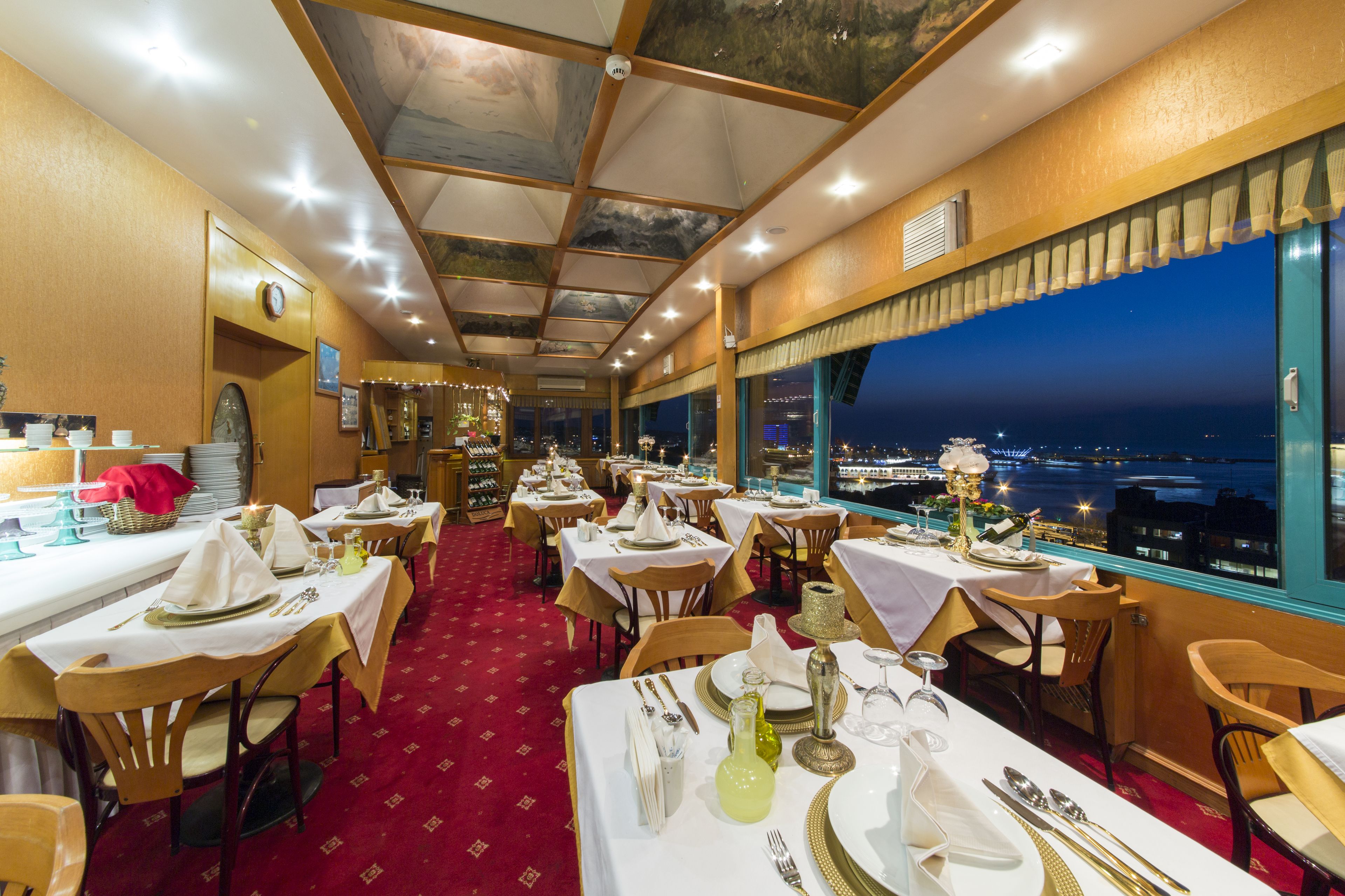 A restaurant with tables set for dining, a red carpet, and a view of the city at night.