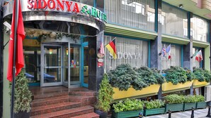 Das äußere Erscheinungsbild des Sidonya Hotels mit Glastür, Stufen zum Eingang und außen an den Fassade aufgehängten Flaggen.