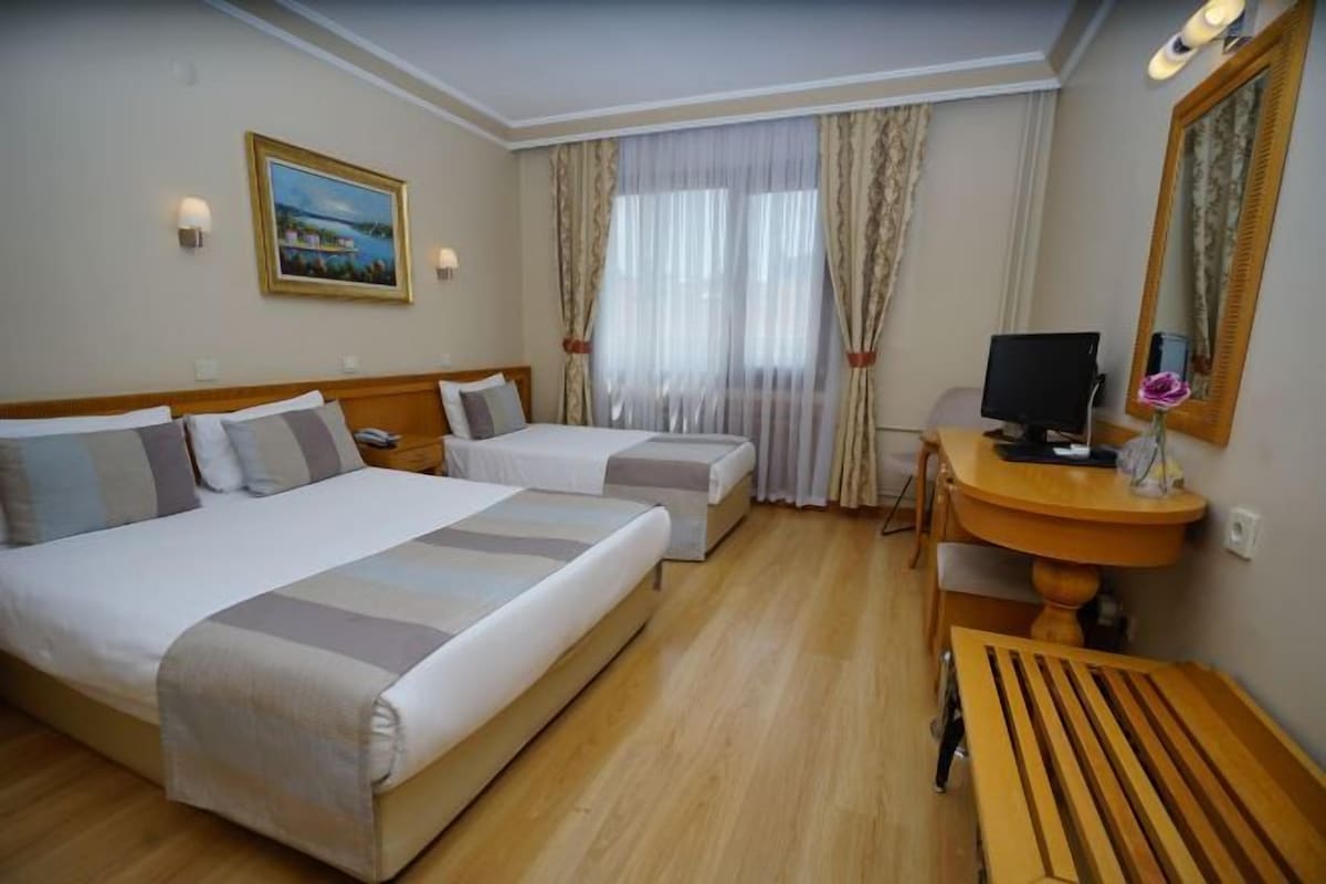 A hotel room with two beds, a desk with a computer, and a window with curtains.