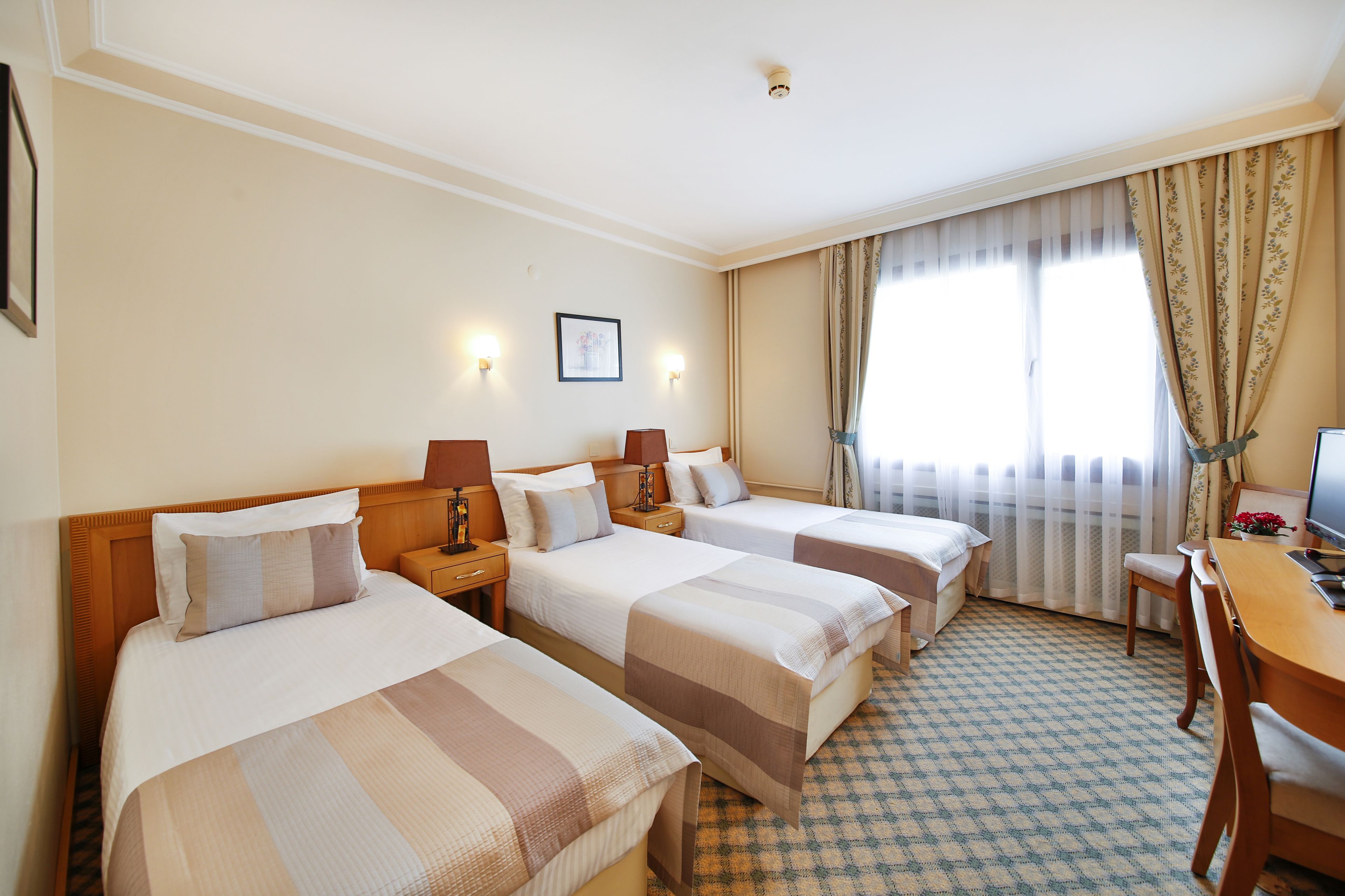 Hotellihuone, jossa on kolme erillistä sänkyä, työpöytä ja tuoli.