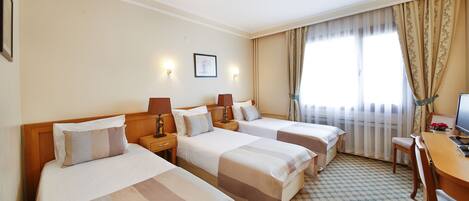 A hotel room with three single beds, a desk, and a chair.