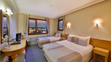 Ein Hotelzimmer mit zwei Betten, einem Schreibtisch mit Computer, einem Stuhl und Blick auf die Stadt.