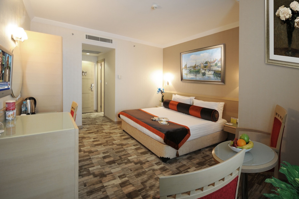 Ein Hotelzimmer mit Bett, Nachttisch, Stuhl und einem kleinen Tisch mit Früchten.