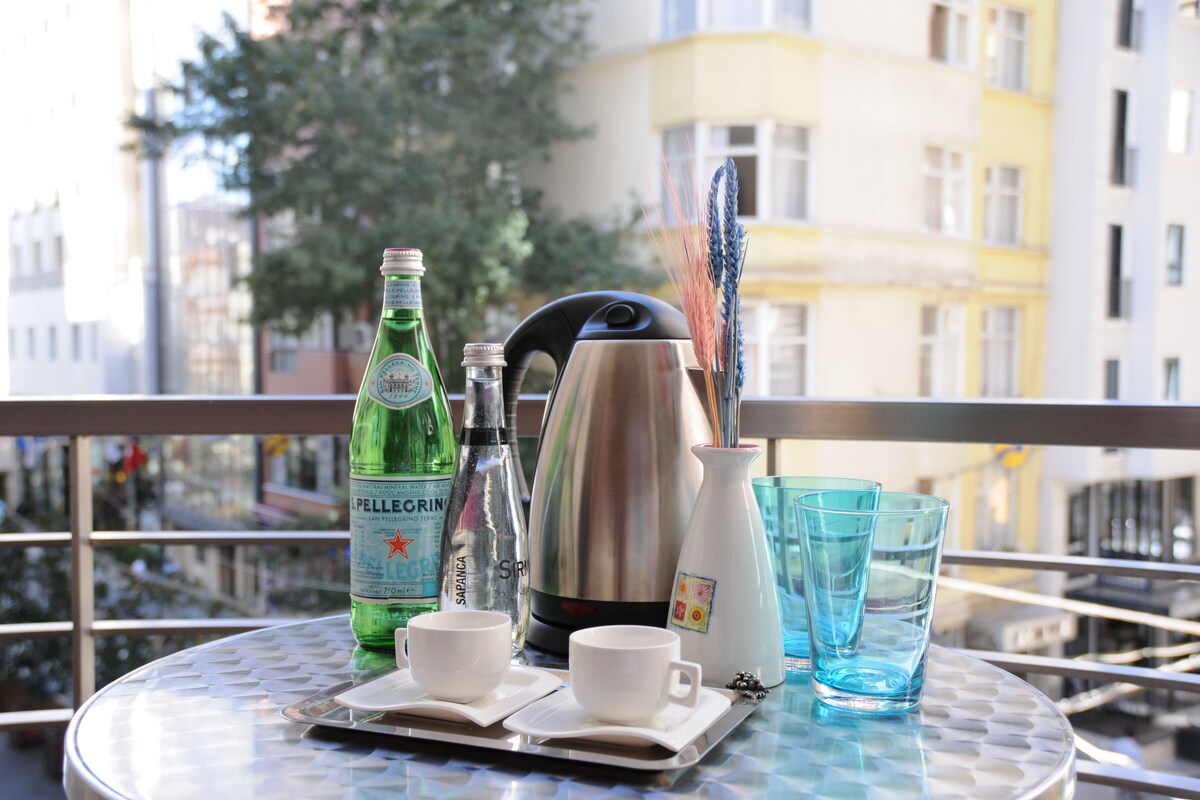Ein Tisch mit einer Pellegrino-Flasche, einem Thermos, einer Kaffeekanne und zwei Tassen auf einem Balkon mit Blick auf die Stadt.