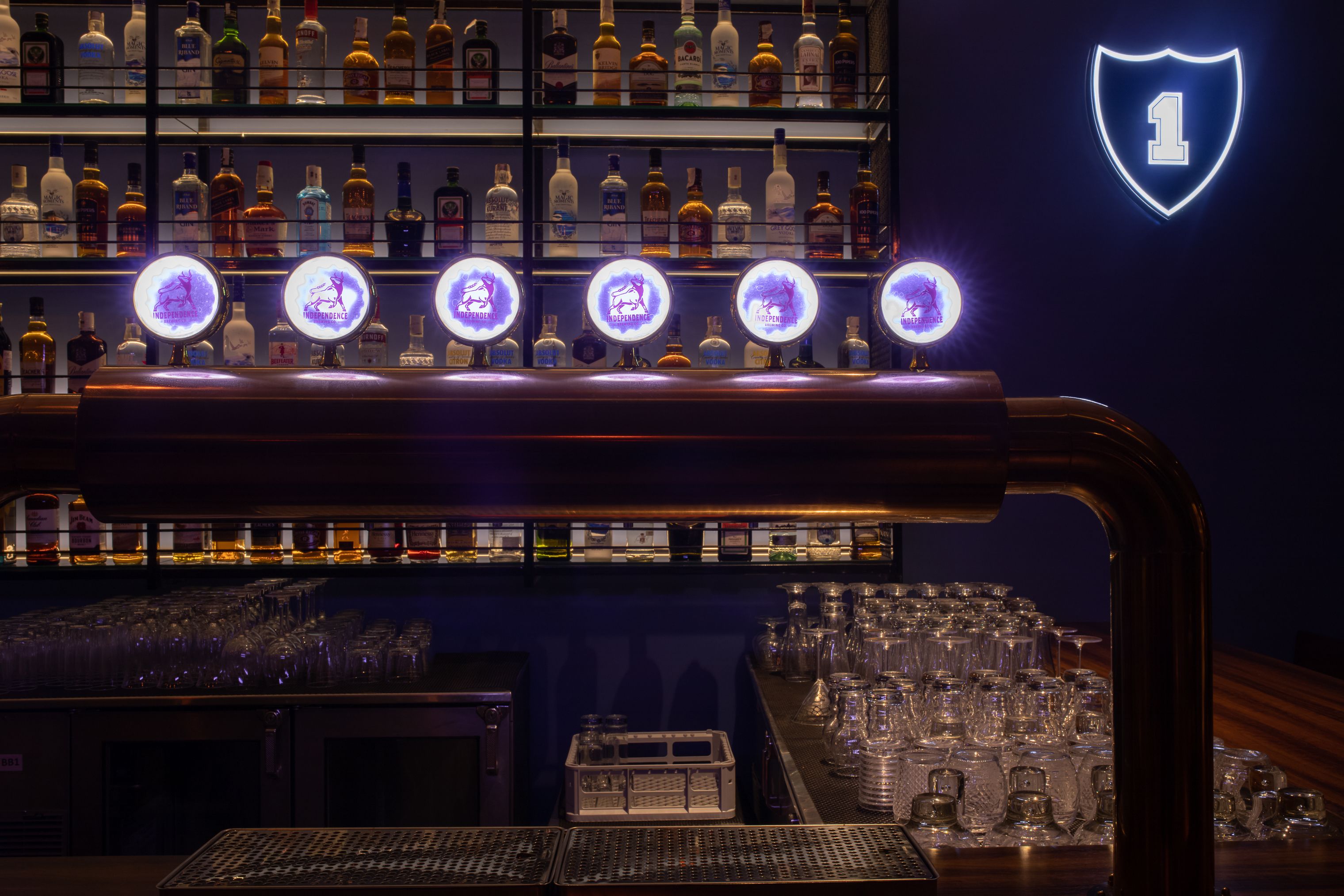 A bar area with shelves of liquor bottles, illuminated bar lights, and a neon sign.