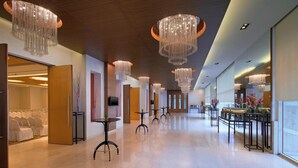 Een ruime hotel lobby met meerdere kroonluchters, tafels en een zithoek met stoelen.