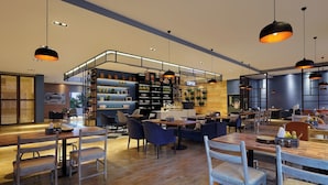 Een modern café met houten tafels en stoelen, een koffiebar en planken met diverse artikelen.