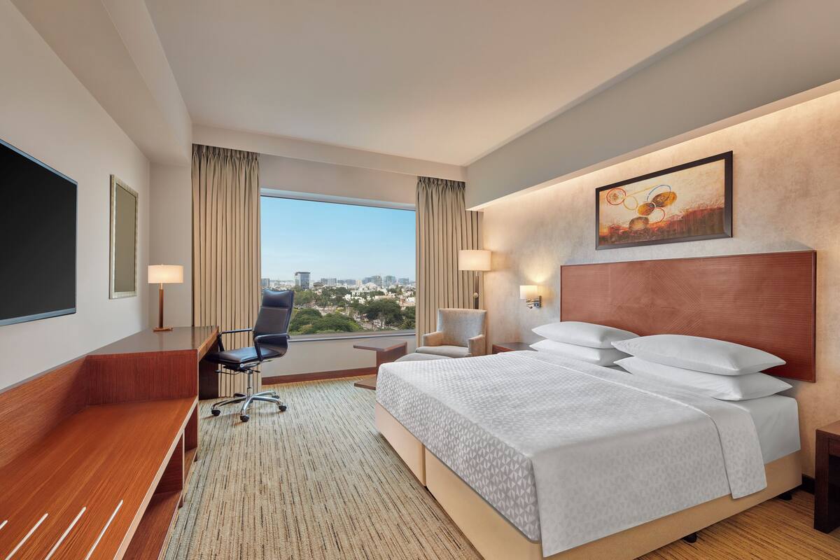 Habitación de hotel con una cama grande, un escritorio, una silla, un televisor y vistas a la ciudad.