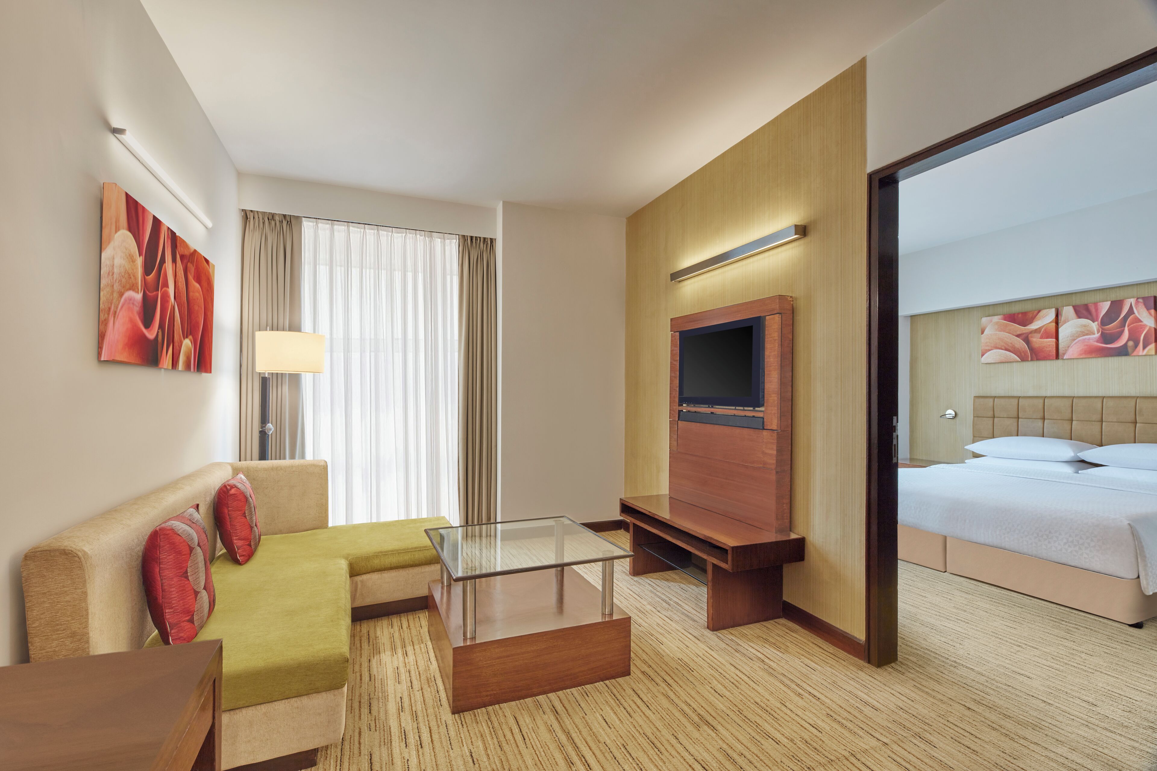 A hotel room with a sofa, a glass coffee table, a TV, and a bed.