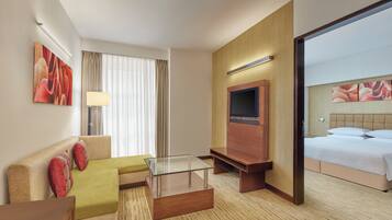 A hotel room with a sofa, a glass coffee table, a TV, and a bed.