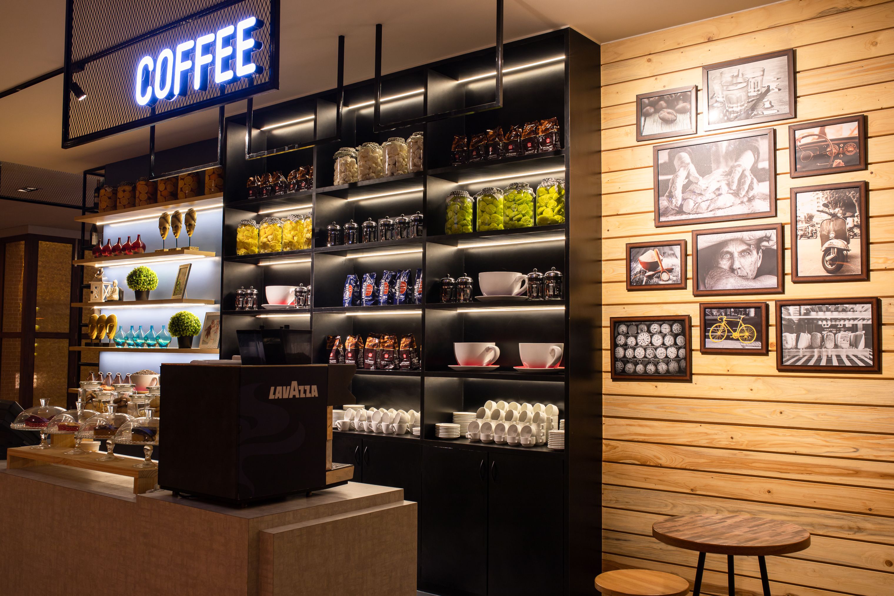 Interior de una cafetería con estantes llenos de granos de café, frascos y tazas.