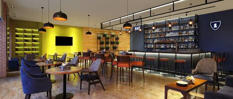 Zona de bar moderna con suelo de madera, taburetes de bar e iluminación colgante. Hay estanterías con botellas y un televisor montado en la pared.