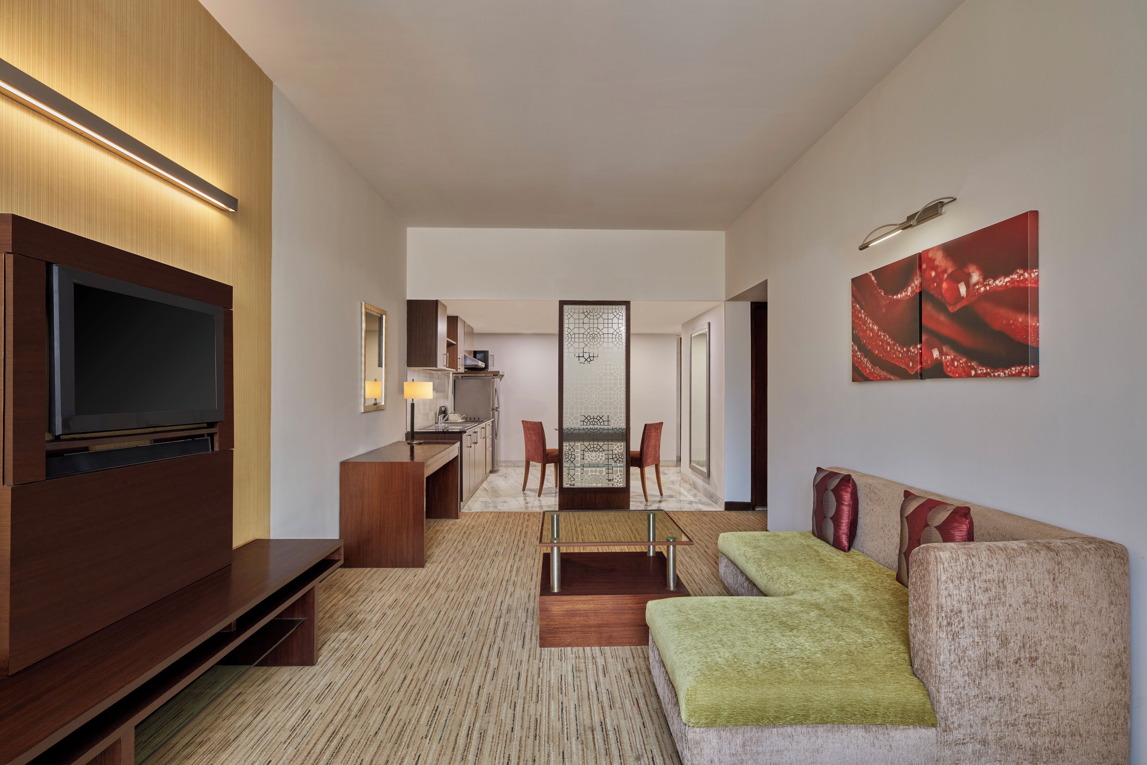 Une chambre d’hôtel moderne équipée d’un téléviseur à écran plat, d’un canapé, d’un coin repas et d’une cuisine en arrière-plan.