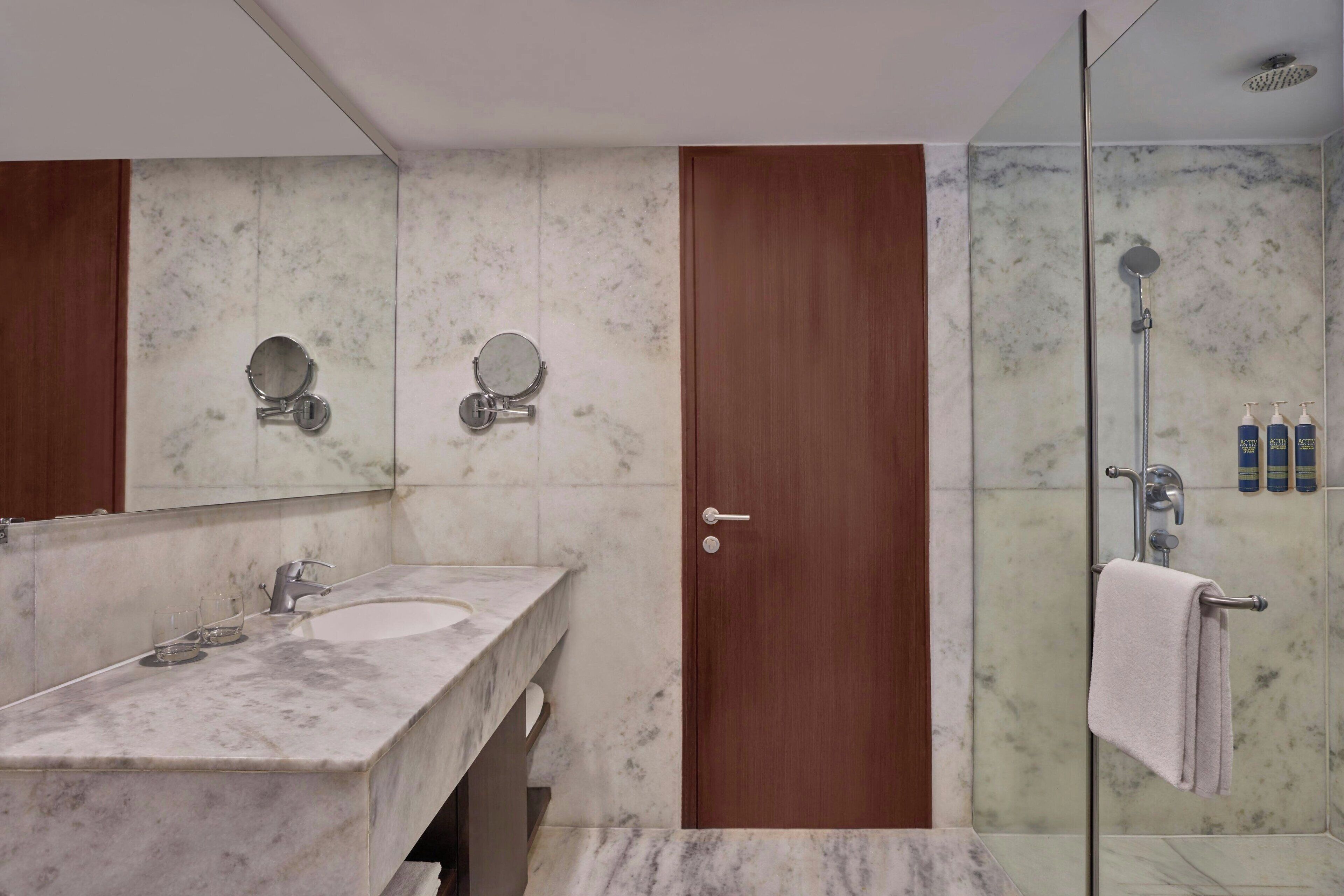 A bathroom with two sinks, a large mirror, a wooden door, and a glass-enclosed shower area.