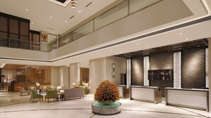 Een moderne hotellobby met een receptiebalie, een zithoek en een decoratieve plantenpresentatie.