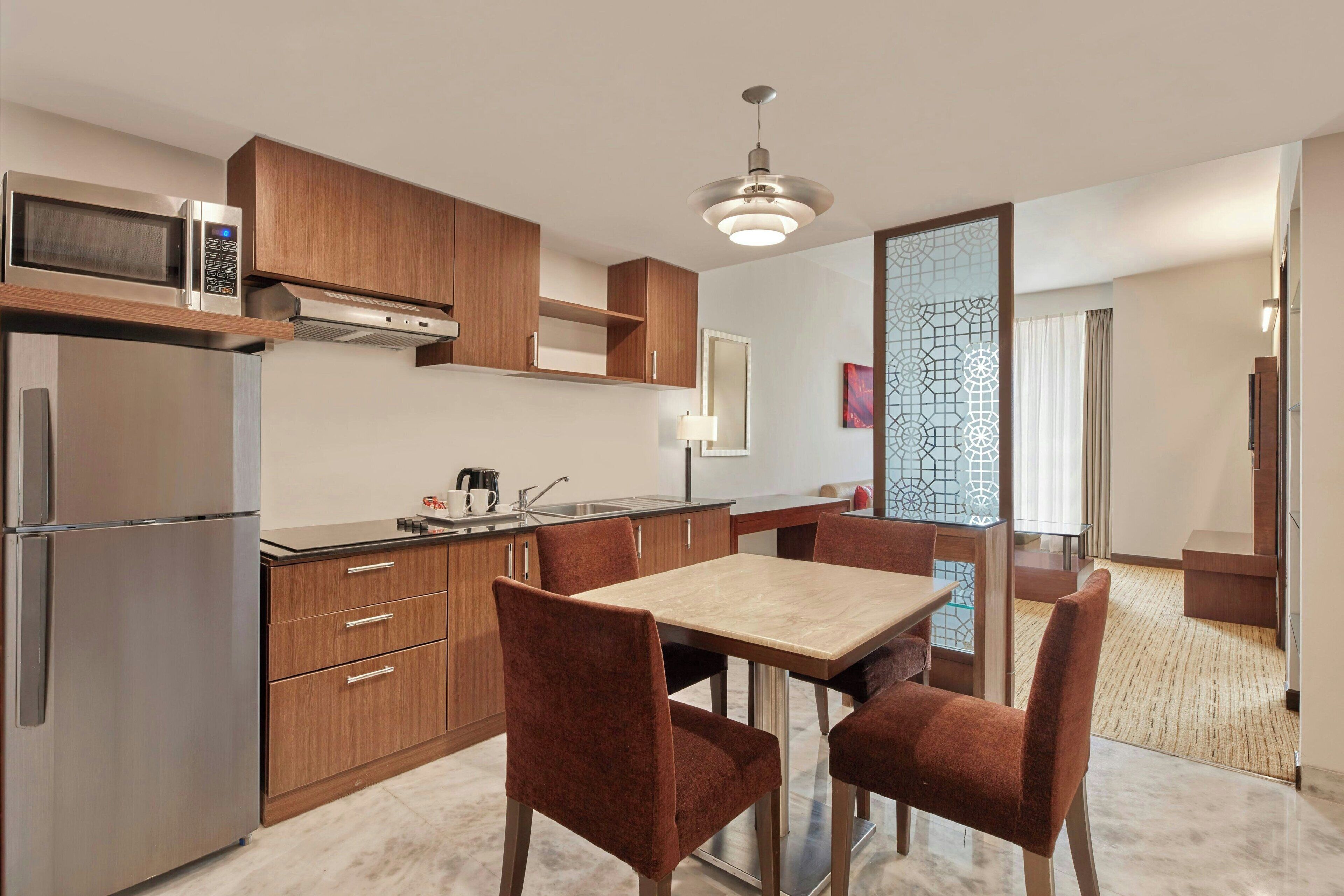 A modern kitchen with stainless steel appliances, wooden cabinets, and a dining area with a marble table and upholstered chairs.