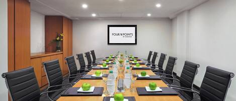 A conference room with a long table, black chairs, and a screen displaying "FOUR X POINTS BY SHEIKATON".
