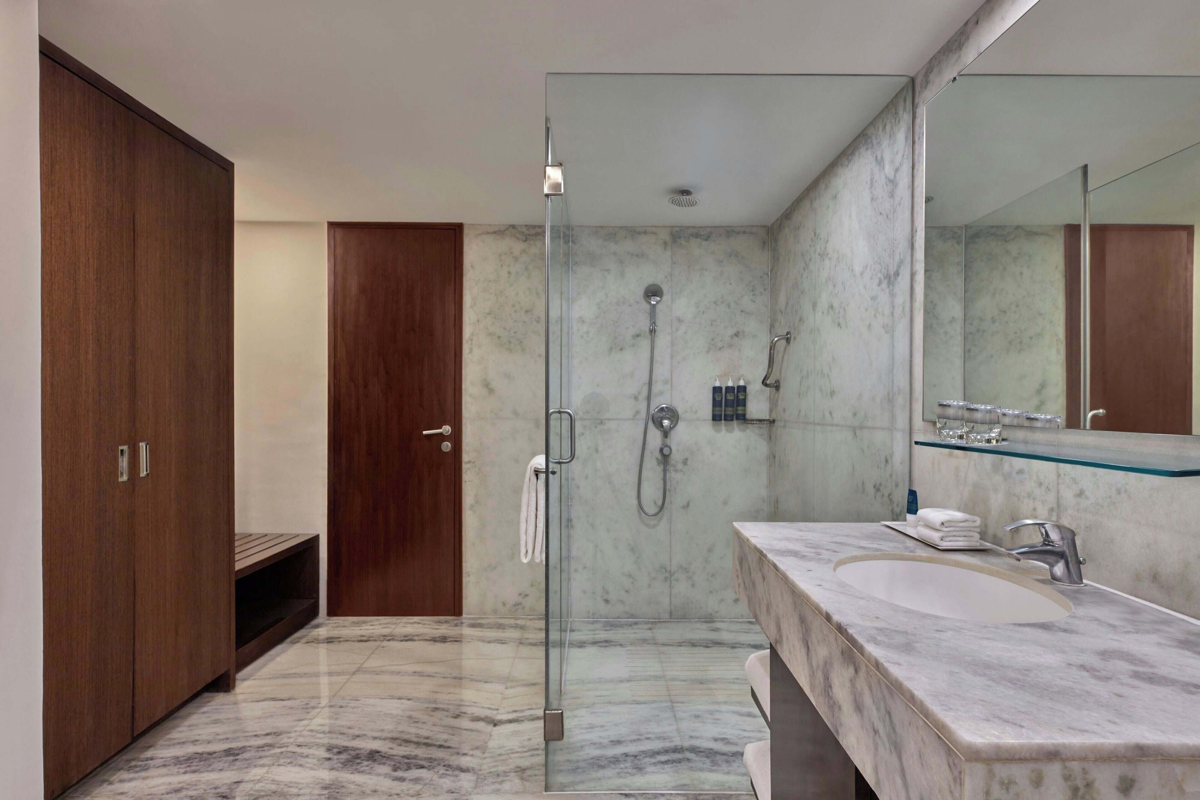 A modern bathroom with a glass-enclosed shower, a marble sink, and wooden cabinets.