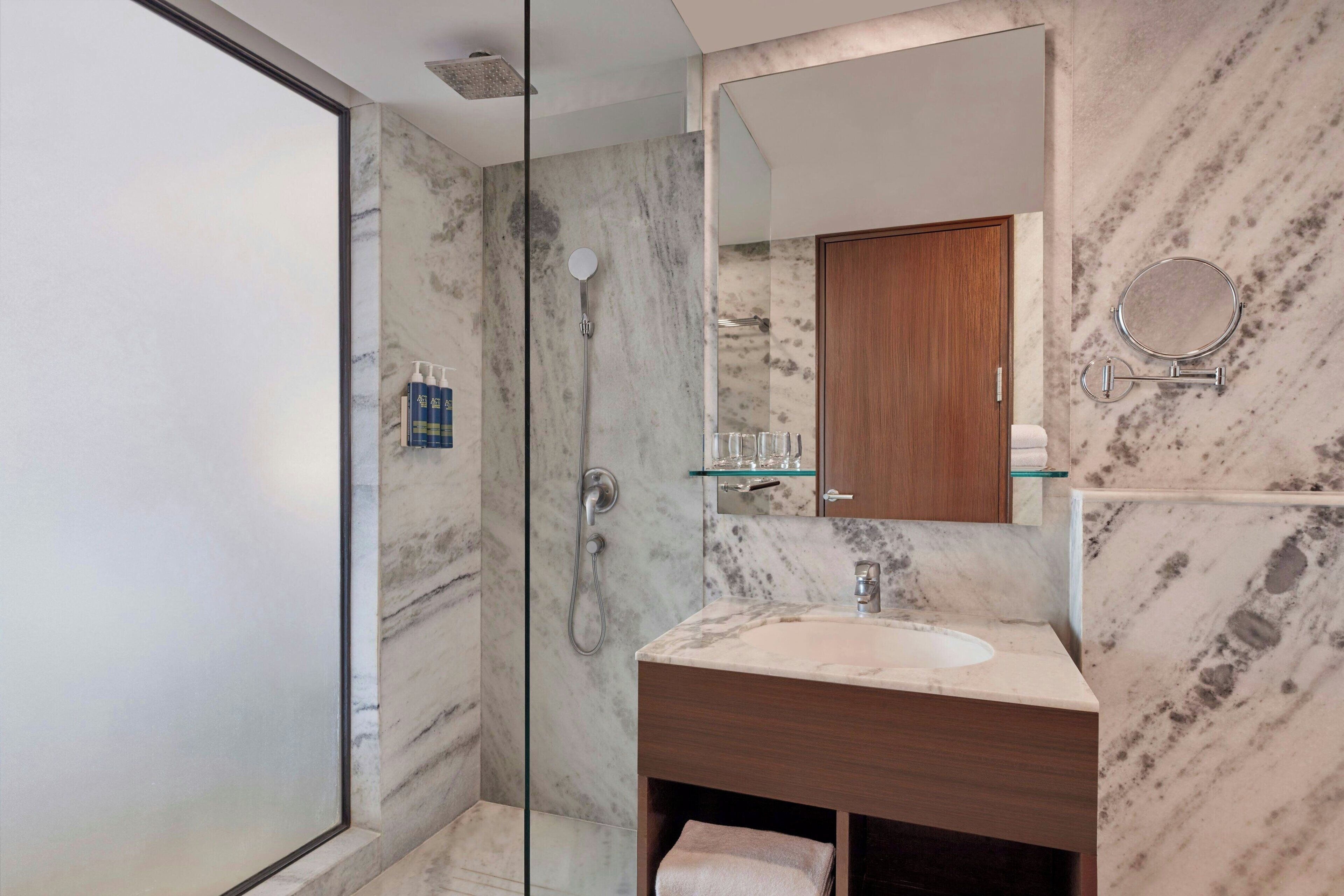 Un baño moderno con cabina de ducha de vidrio, pared con azulejos de mármol, tocador de madera y un espejo grande.