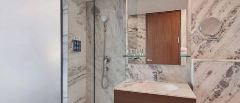 Un baño moderno con cabina de ducha de vidrio, pared con azulejos de mármol, tocador de madera y un espejo grande.