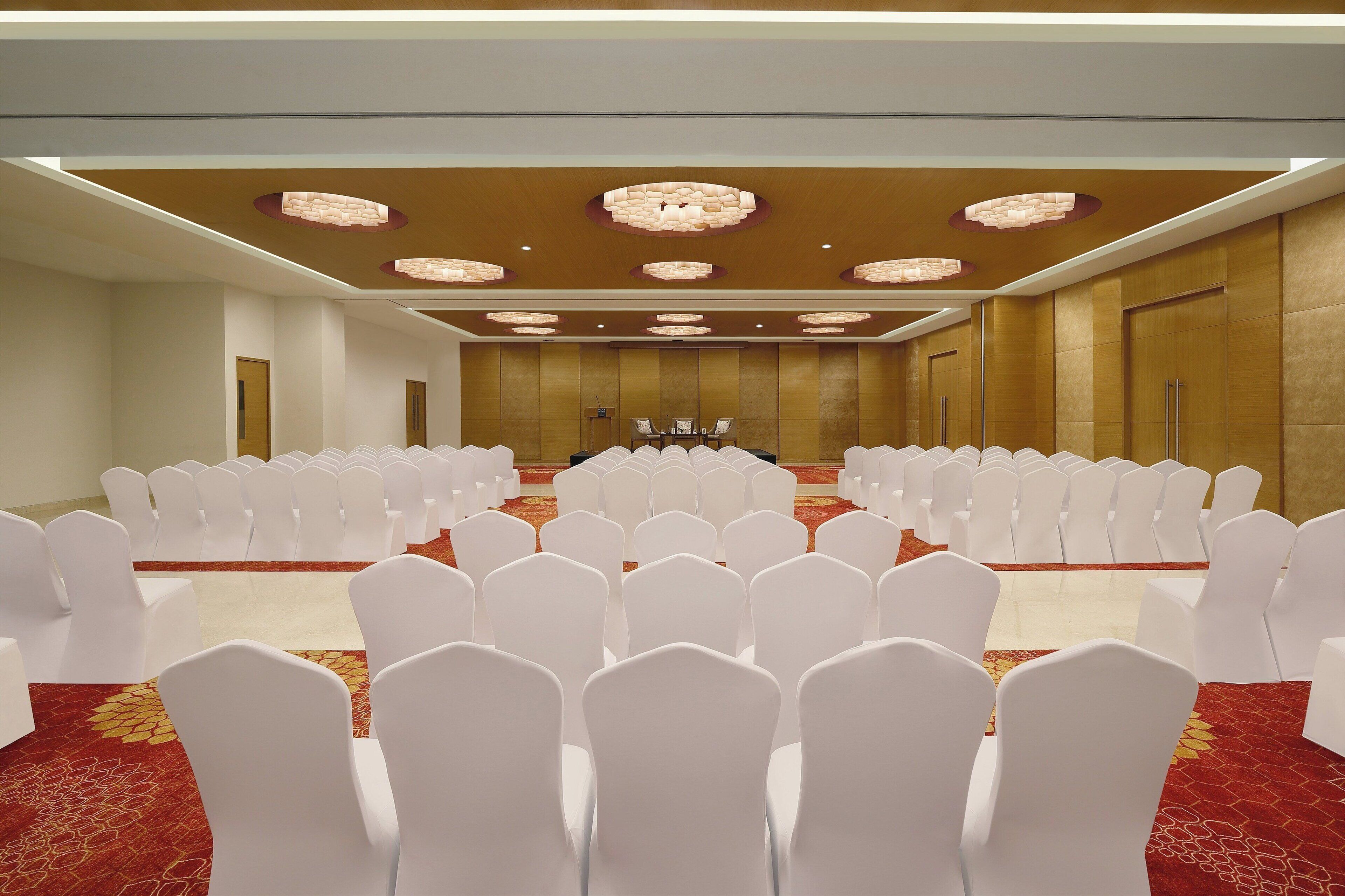 A conference room with rows of white chairs and a stage at the front.