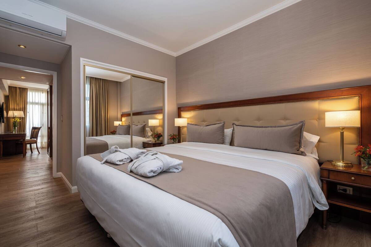 A hotel room with a large bed, bedside lamps, a mirror, and a desk with a chair.