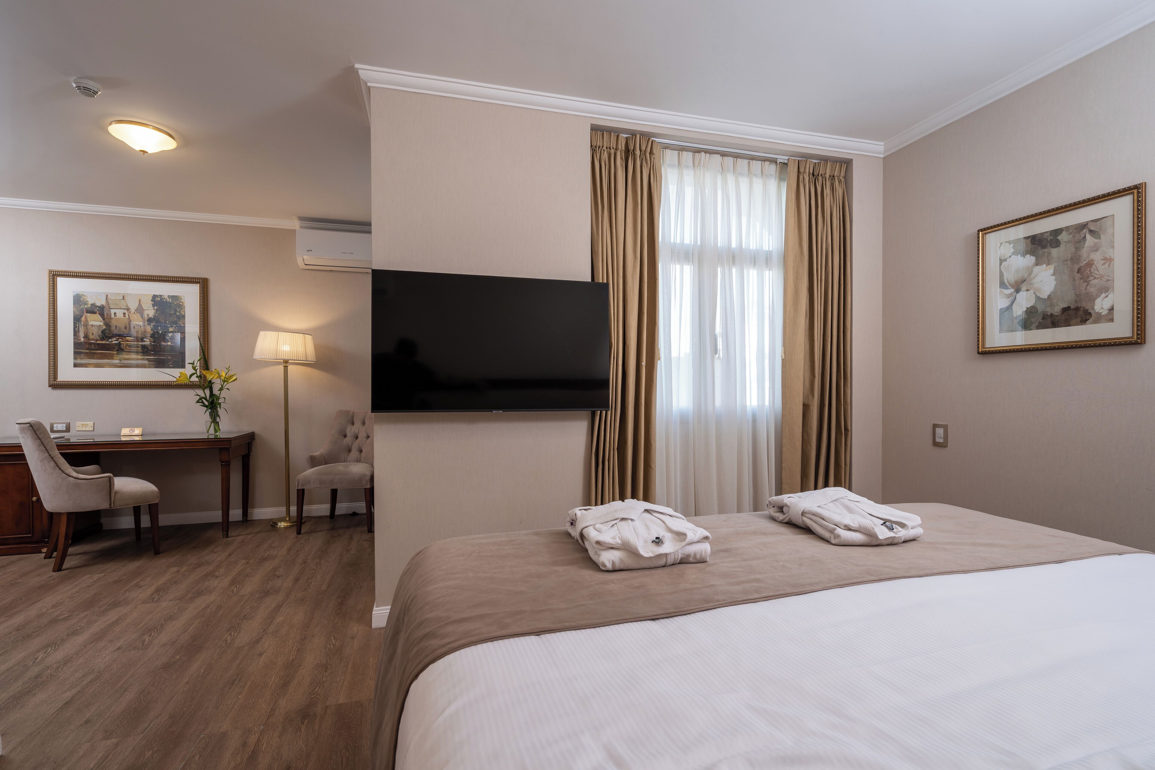 A hotel room with a bed, a desk, a chair, a flat-screen TV, and a window with curtains.