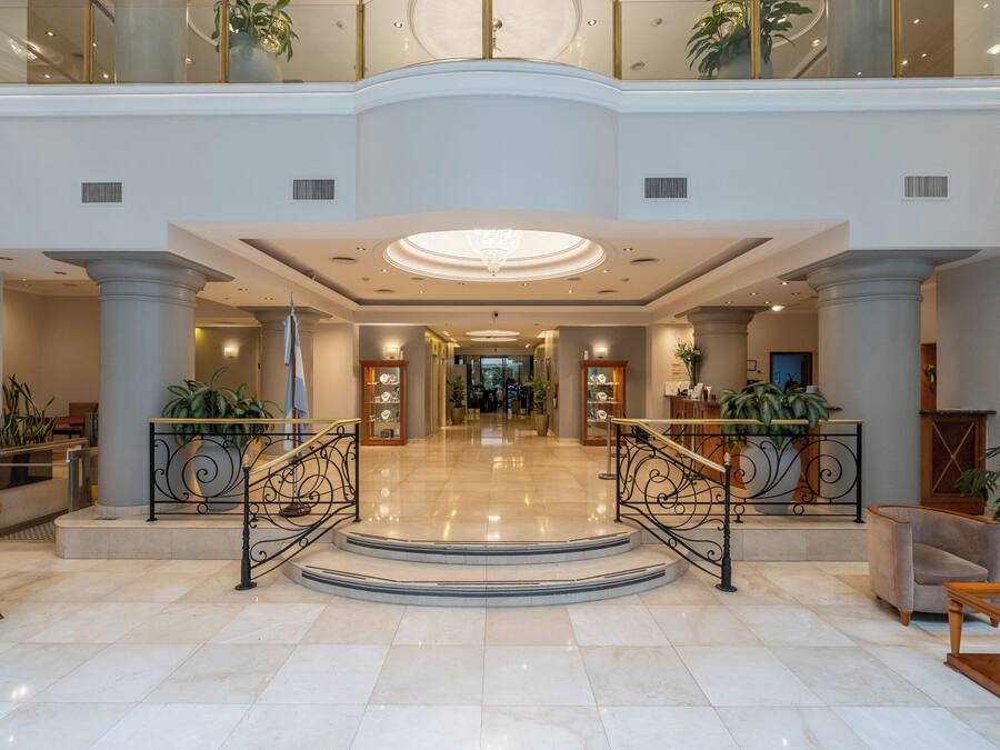 Un hall espacioso con una escalera central, amplias columnas y plantas en macetas.