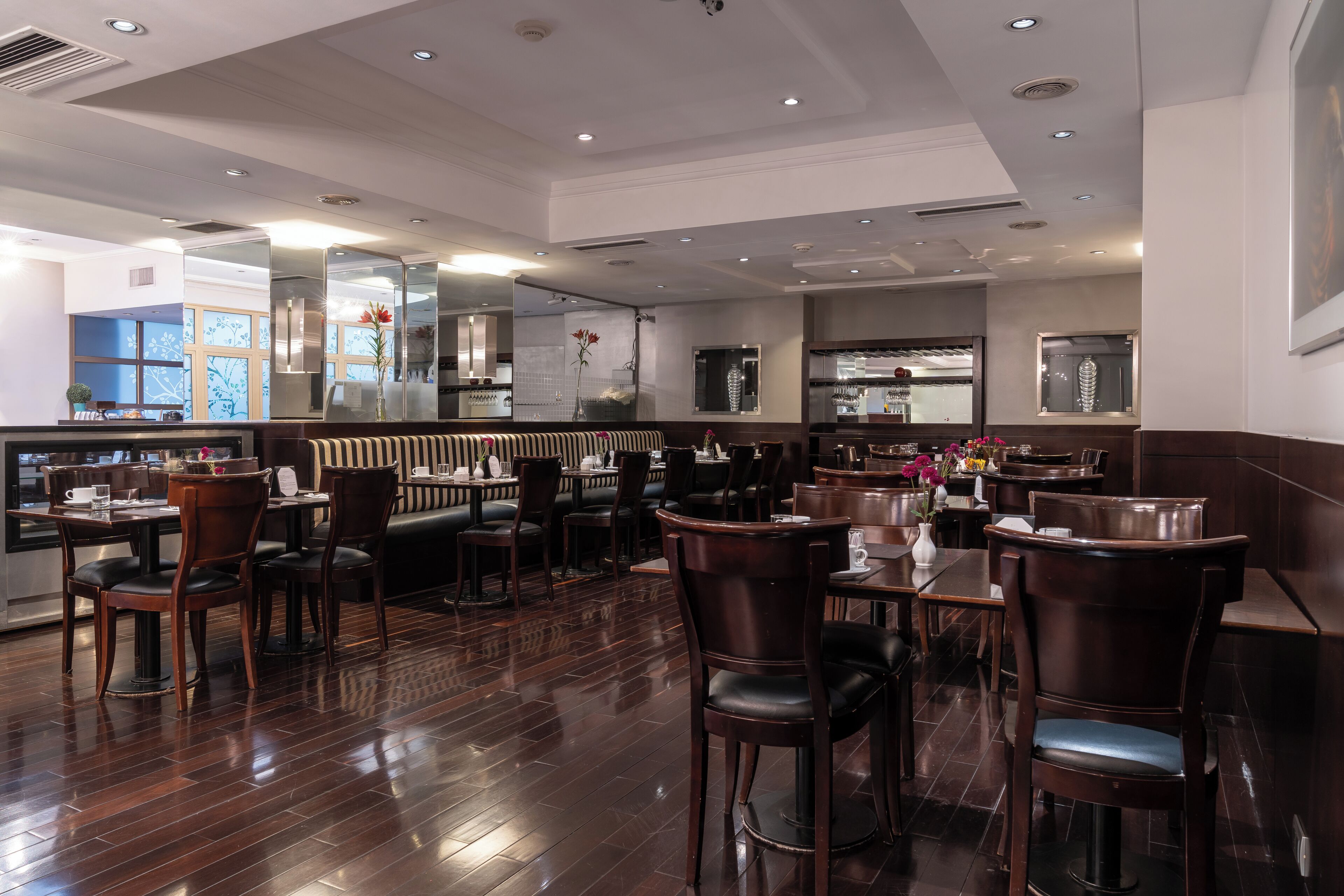A restaurant with wooden flooring, dark wooden chairs, and tables. There are glass partitions separating dining areas.