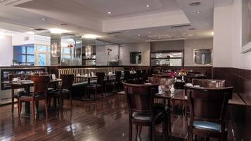 A restaurant with wooden flooring, dark wooden chairs, and tables. There are glass partitions separating dining areas.