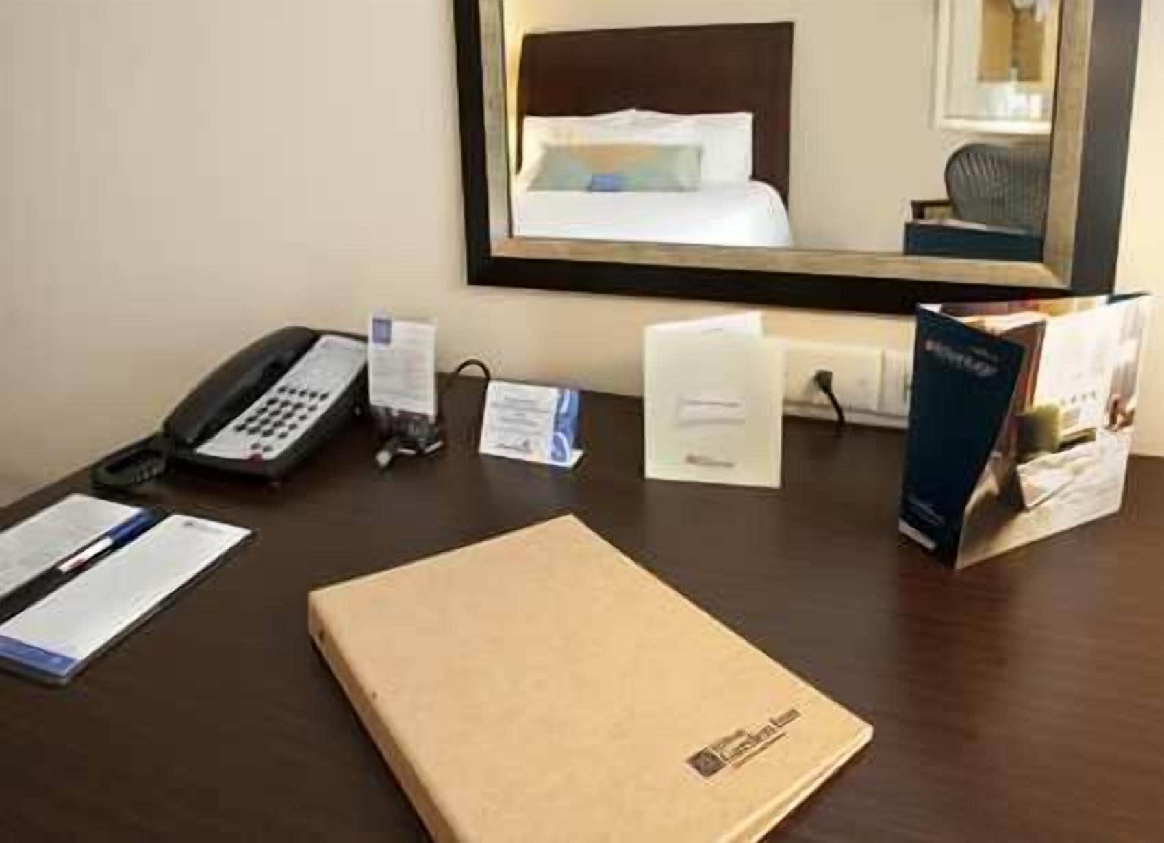 Habitación de hotel con una cama, teléfono, escritorio con una computadora portátil, folleto y una mesita con una taza y una caja de pañuelos.