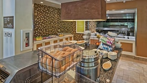 A buffet setup with a toaster oven, a variety of food items, and a large kitchen area in the background. - Hilton Garden Inn Mount Laurel Philadelphia (Mount Laurel)