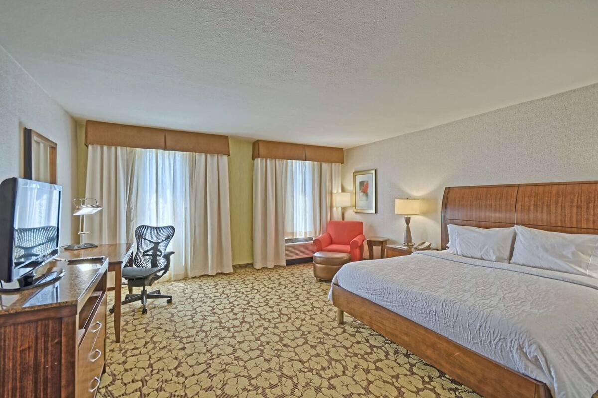 A hotel room with a bed, desk, chair, and a television.