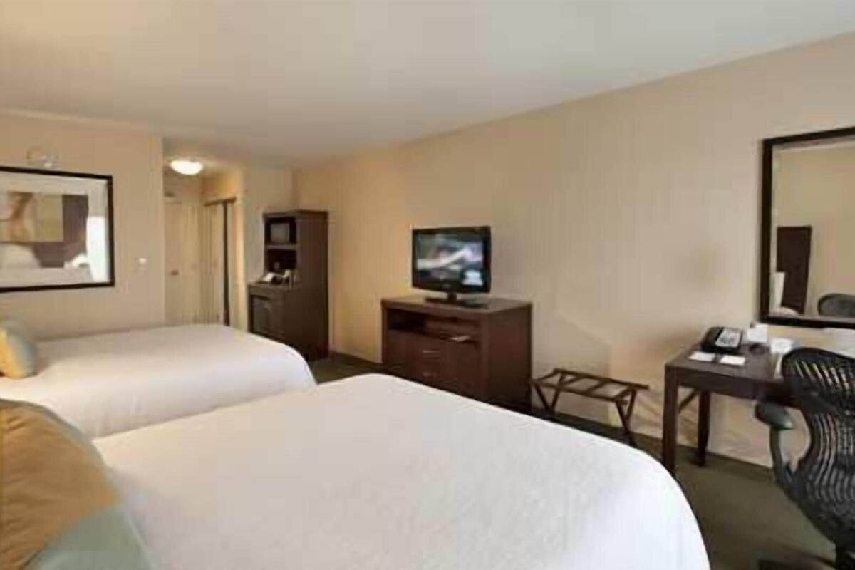 A hotel room with two beds, a TV, a desk with a chair, and a mirror.