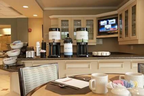 A hotel kitchen with a coffee station, a television, and a dining area with chairs and a table.