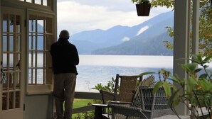A man standing by a window overlooking a lake with mountains in the background.