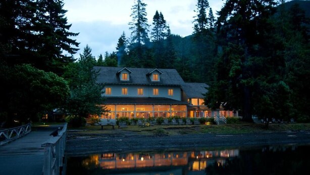 A large, two-story lodge with a reflective pool in front, surrounded by dense forest.