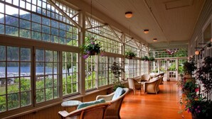 A spacious room with large windows overlooking a lake, wicker furniture, and hanging plants.