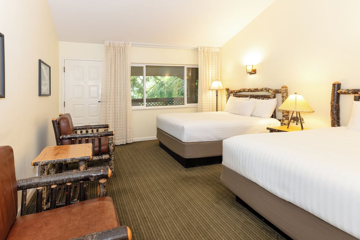 A hotel room with two beds, a wooden chair, a desk, and a window with curtains.