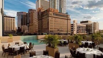 A rooftop dining area with tables set for guests, overlooking a cityscape with various buildings and a clear sky.