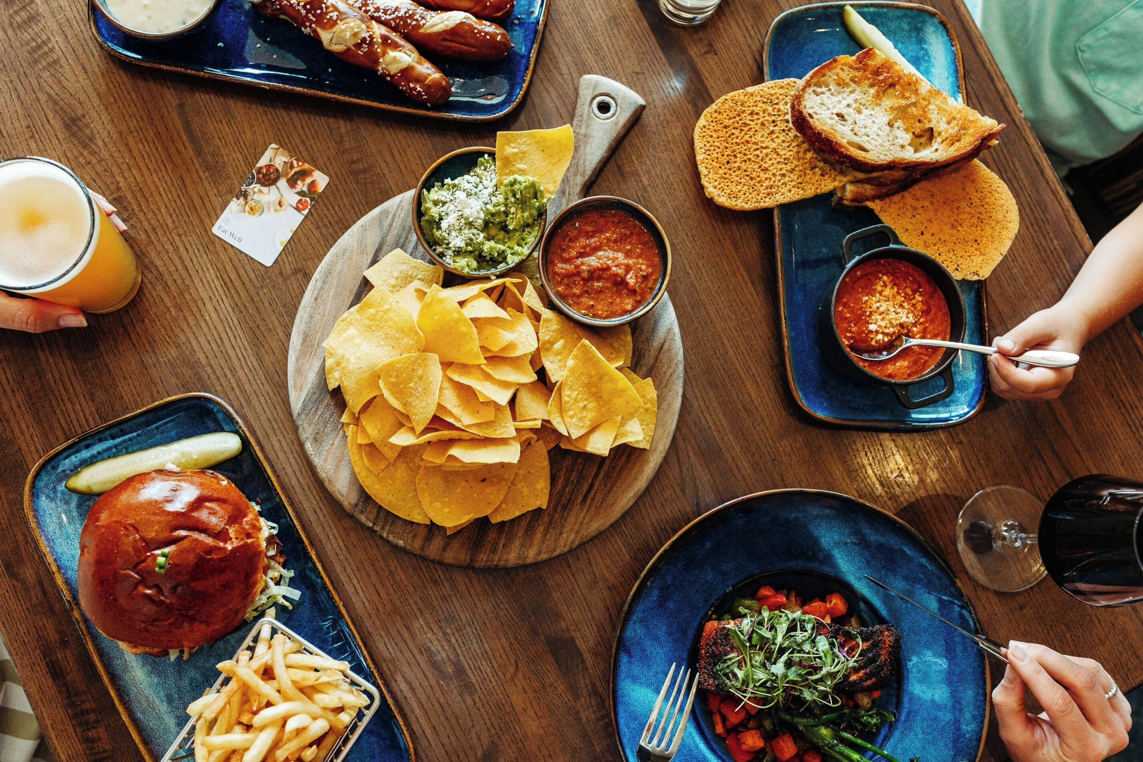 A dining table with various dishes including nachos, a burger, and a steak with vegetables.