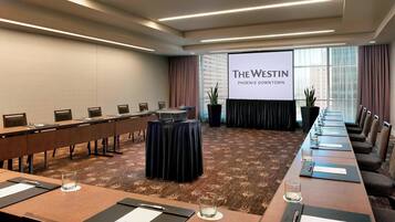 A conference room with a long table, chairs, a podium, and a screen displaying "The Westin Phoenix Downtown".