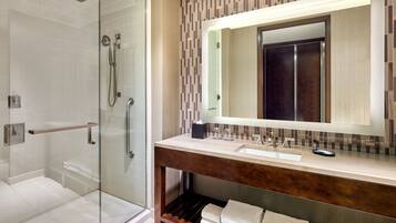 A modern bathroom with a glass-enclosed shower, a wooden vanity with a large mirror, and neatly arranged towels.