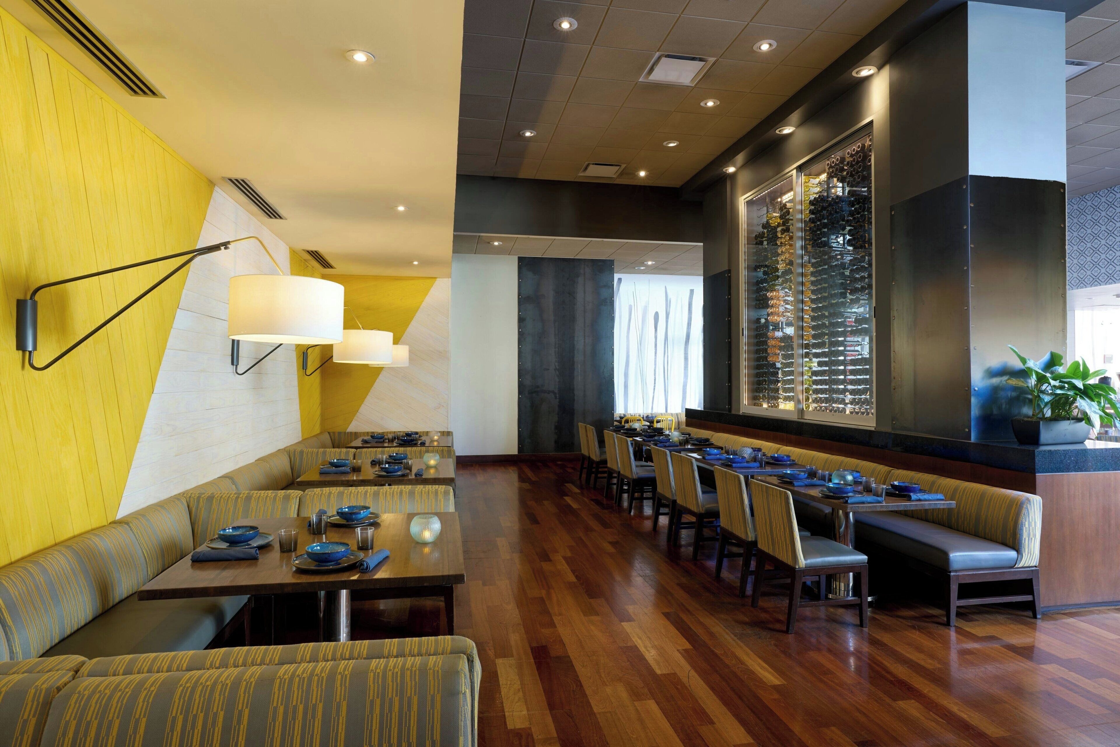 Un espace repas moderne avec des banquettes et des tables, un plancher en bois et un grand meuble à vin.