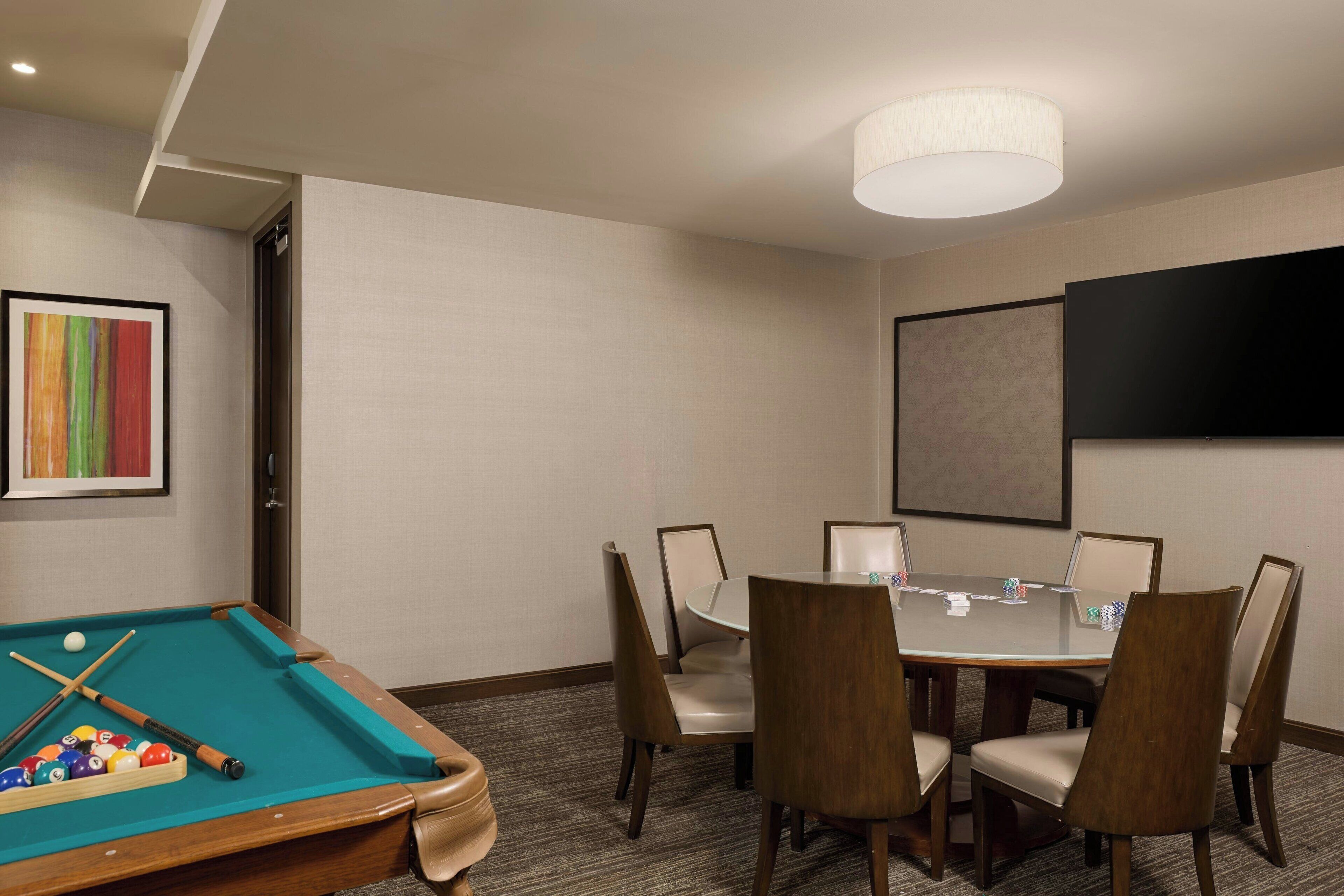 A conference room with a pool table, a round table with chairs, and a flat-screen TV on the wall.