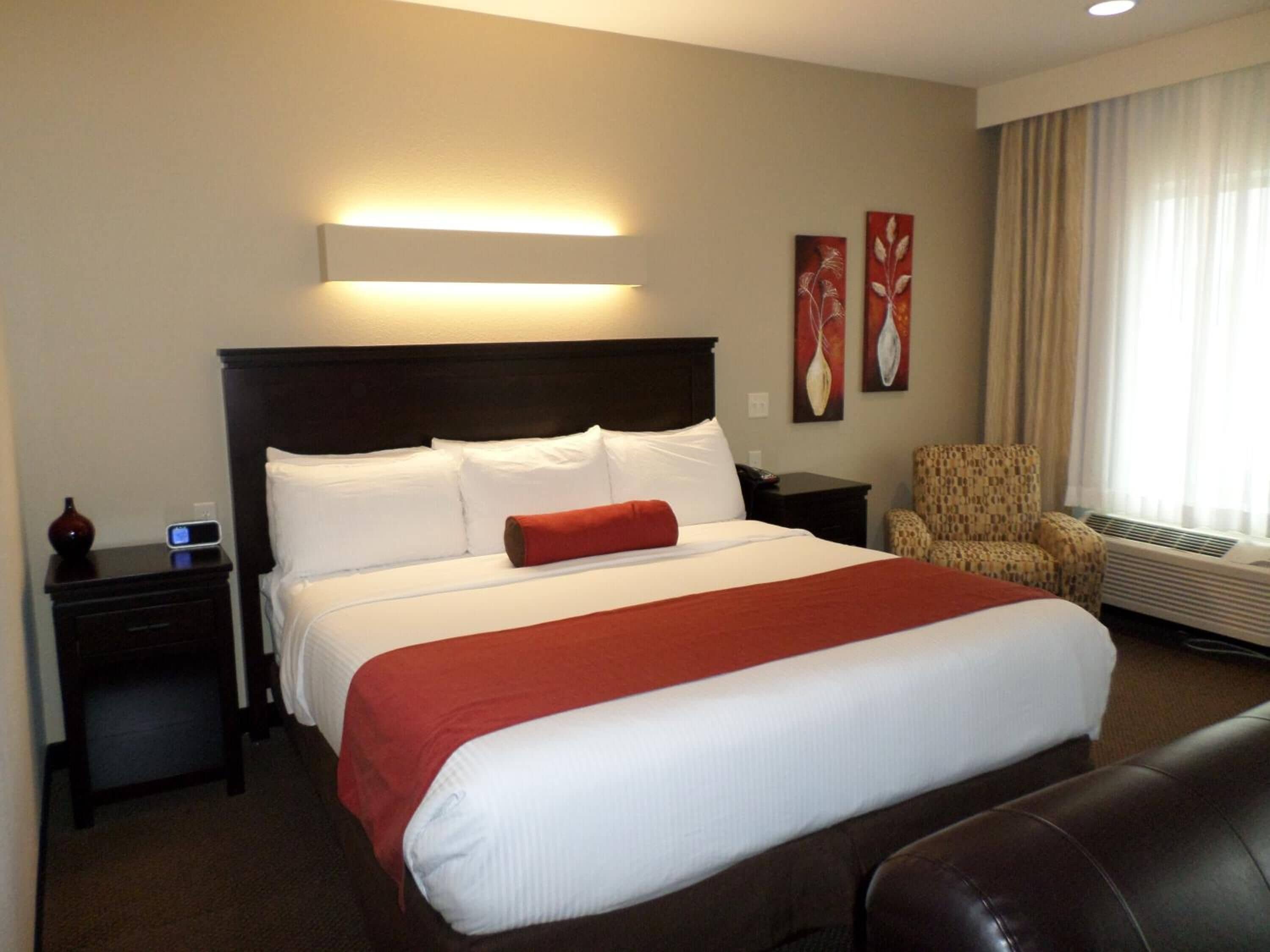 Una habitación de hotel con una cama grande, una mesita de noche, una silla y una lámpara fijada en la pared.
