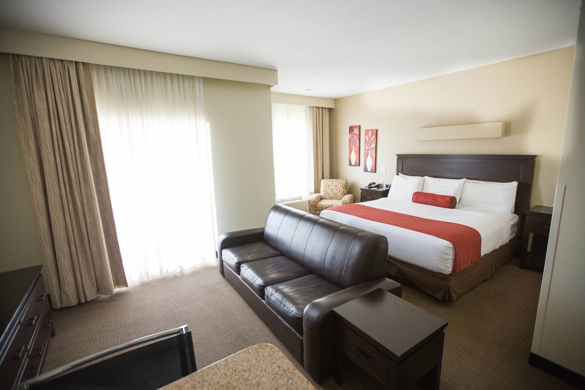 Una habitación de hotel con una cama, un sofá de cuero, una mesita y una silla.
